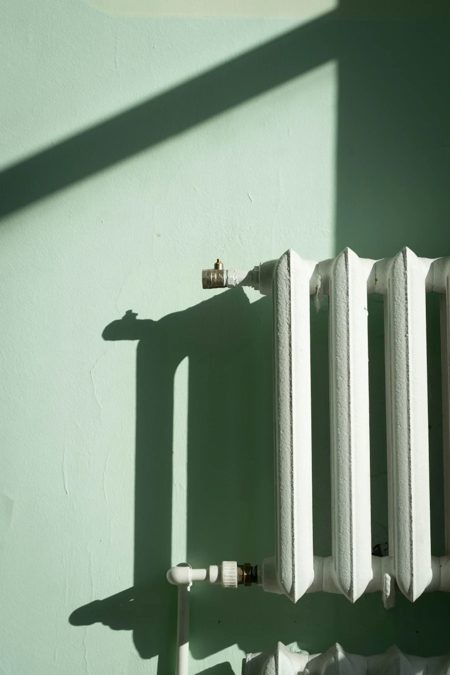 White radiator against a pale green wall in the sunlight